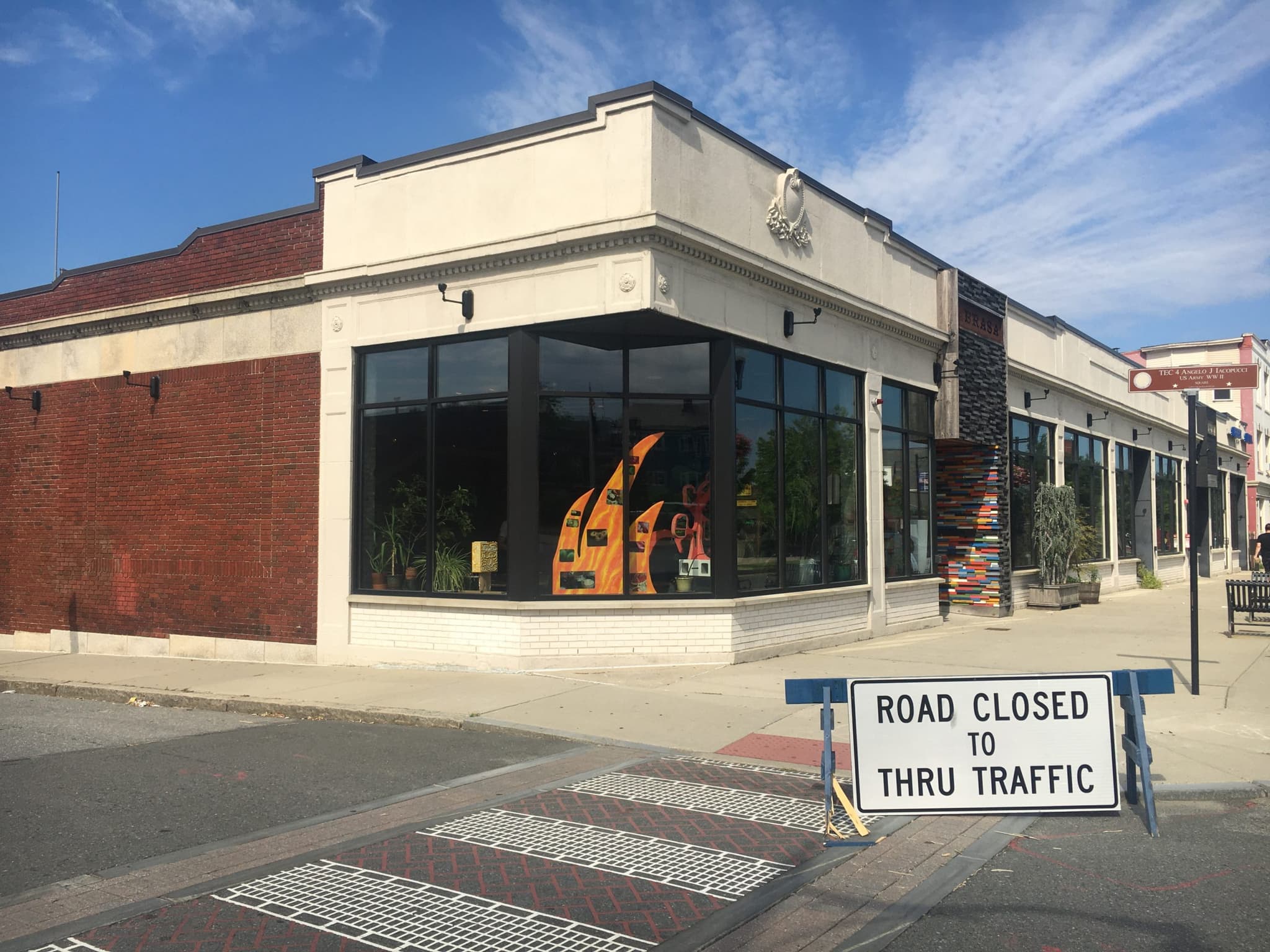 Works are displayed in the window of La Brasa restaurant, while a road closing sign appears on the street nearby.