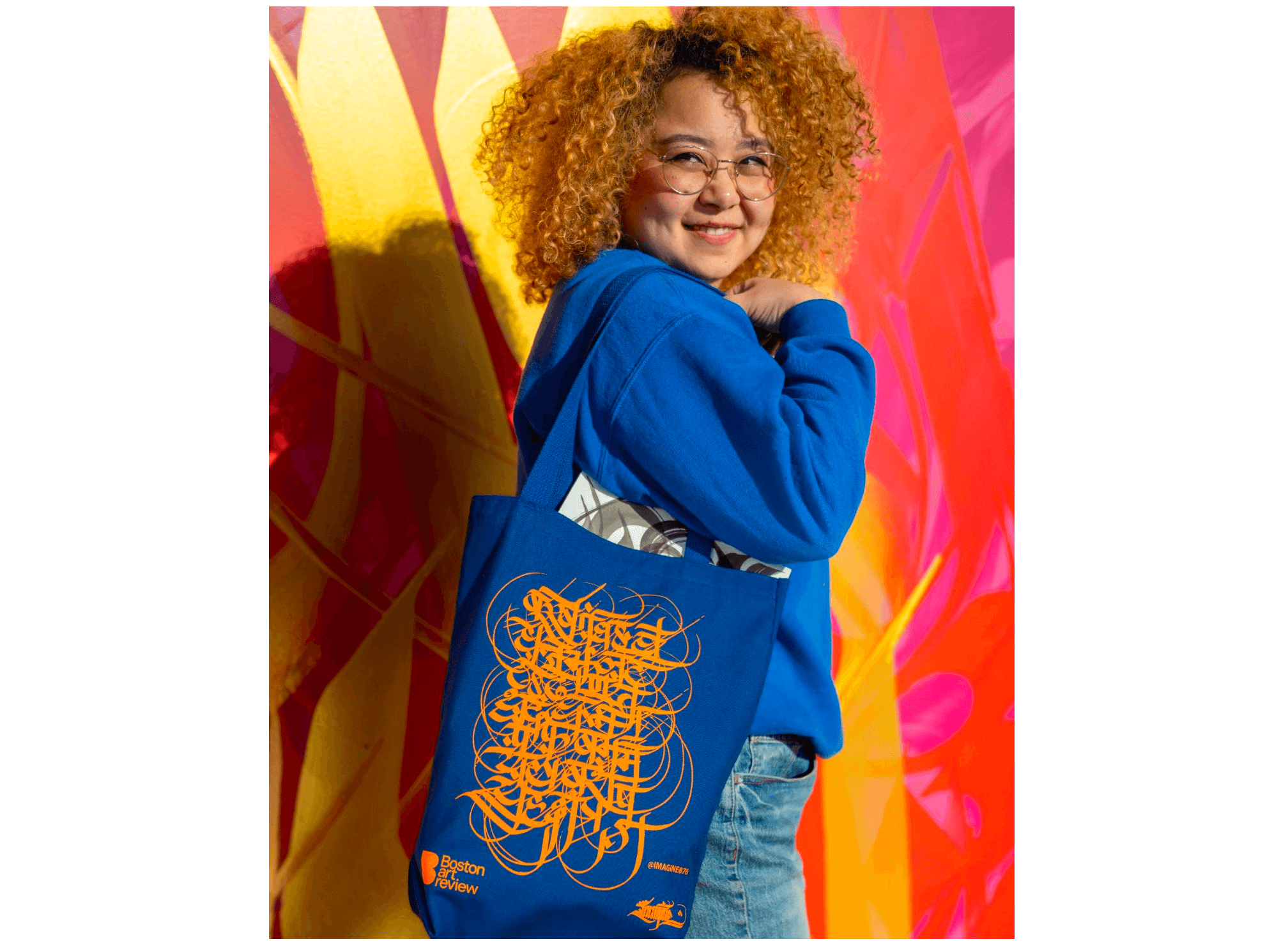 Sneha Shrestha, a young woman with her hair dyed blond, models her blue and orange tote collaboration with Boston Art Review.